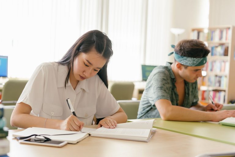 Two students writing at tables in a library